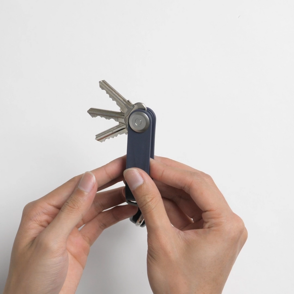 Dos manos sujetan el llavero organizador Orbitkey Active azul y muestran tres llaves desplegadas.